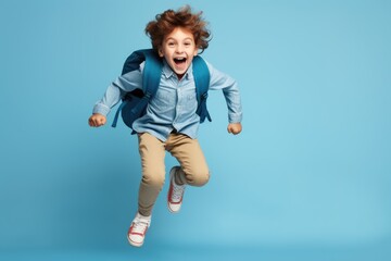 smiling little boy with backpack jumping on blue background - obrazy, fototapety, plakaty