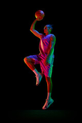 Full-length image of young man, basketball player in uniform in motion, jumping with ball against...