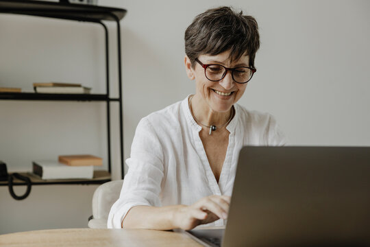 Smiling stylish mature business woman using laptop sitting at workplace desk.