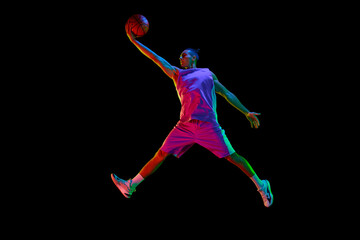 Slam dunk. Winning goal. Teen boy playing basketball, throwing ball in a jump against black studio...