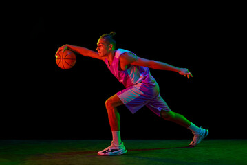 Muscular, active young man in motion, basketball player with ball during game against black...