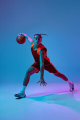 Concentrated young guy in sportswear playing basketball, training dribbling ball exercises on blue...