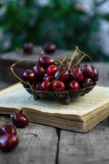 Ripe fresh cherries in vintage vase on old book on rustic wooden background