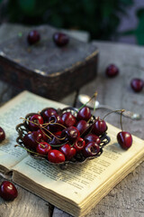 Ripe fresh cherries in vintage vase on old book on rustic wooden background