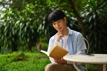 Fototapeta premium A young Asian man reading a book while sitting in the garden