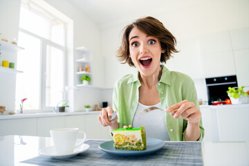 Obraz na płótnie Canvas Photo of positive shocked girl wear green shirt cutting fresh piece of cake indoors kitchen room