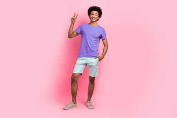 Full size photo of satisfied guy with perming coiffure wear stylish t-shirt arm in pocket show v-sign isolated on pink color background