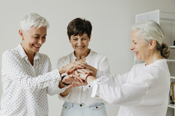 Three confident mature women stacking hands and smiling.