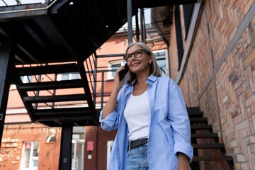 a mature gray-haired woman in a summer outfit walks around the city and chats on the phone