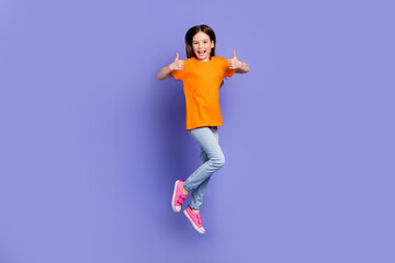 Fototapeta na wymiar Full length photo of satisfied schoolkid dressed orange t-shirt flying showing thumbs up nice work isolated on purple color background