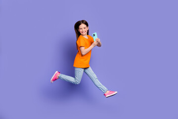 Full length photo of hurry running schoolkid dressed orange t-shirt flying hold smartphone running isolated on purple color background