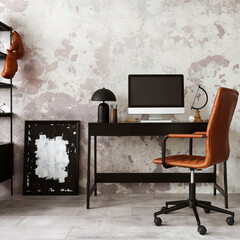 Concrete interior of home office with black desk, brown armchair, computer screen, office accessories and lamp. Rack with personal accessories. Home decor. Template.
