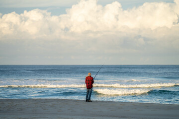 man beach fishing in the ocean waves at dusk