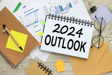 OUTLOOK 2024 stationery and calculator on financial chart. text on notepad page with spiral