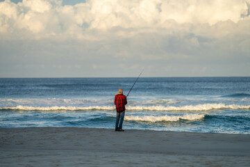 man beach fishing in the ocean waves at dusk