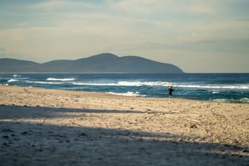 Fototapeta na wymiar man beach fishing in the ocean waves at dusk