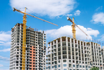 A tower construction crane on the background of a blue sky with clouds. The frame of a building under construction. Building construction. Load-bearing reinforced concrete walls of the house.