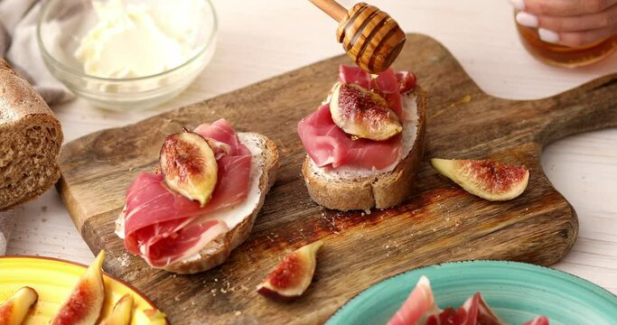 The process of making a sandwich with prosciutto and figs. Women's hands drizzled with honey italian appetizer. close-up of food preparation.