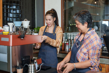 Beautiful daughter barista prepares to make coffee for customers as retire elderly mother takes orders. in front of coffee machine Behind counter in cafe shop. The owner of small business coffee shop