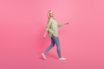 Fototapeta na wymiar Profile side full length photo of cheerful glad lady dressed stylish clothes laughing going empty space isolated on pink color background