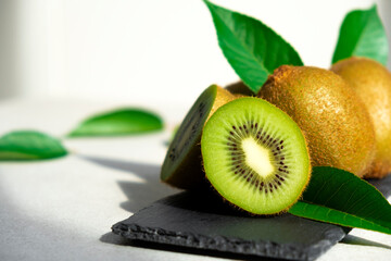 Ripe kiwi fruits in sunlight. Heap of whole kiwi fruits with green leaves and fresh cut kiwi on...