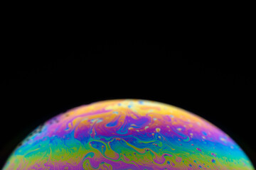 Colorful close-up of soap bubble on black background, iridescence phenomenon, looks like rising planet