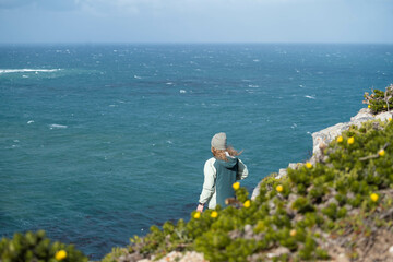 Fototapeta na wymiar Woman standing on a rock onto of a cliff looking out at the view of the ocean 