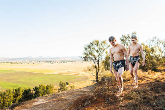 Two Aboriginal Australians on country walking along the edge of a cliff with view over farmland