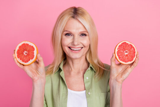 Portrait of pretty aged lady toothy smile good mood hands hold two halves grapefruit isolated on pink color background