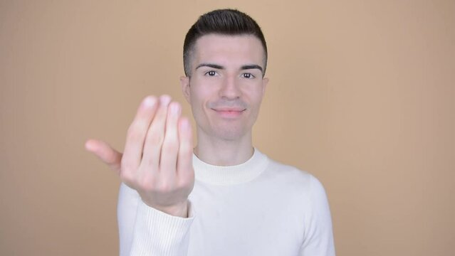 Man waves hand, inviting the viewer closer on isolated background. Male model showing 'Come To Me' gesture. Young handsome caucasian.
