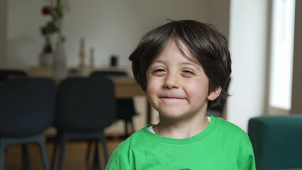 Joyful little boy smiling at camera standing indoors at home. Portrait of a handsome child, close-up face with friendly emotion