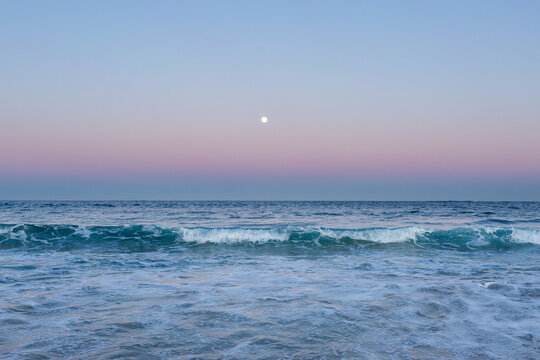 Full moon rising in dusk light over ocean seawater
