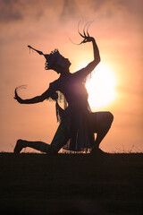 Nora performs dance moves in the field at sunset.beautiful sky background..The sun casts a silhouette on Nora..Nora is a form of traditional, folk performing arts in the southern region of Thailand..