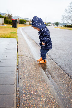 Toddler girl wearing raincoat splashing in gutter at roadside