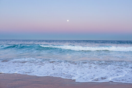 Full moon rising in dusk light over ocean and sandy seashore 