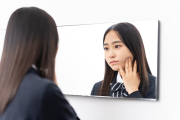 鏡を見ている日本人女子高校生/肌を触っている