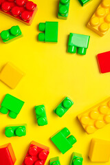 Children's plastic multi-colored constructor on yellow background, top view. Game for children, toddlers, building blocks, bricks, toys, child development, co-creation. Flat lay