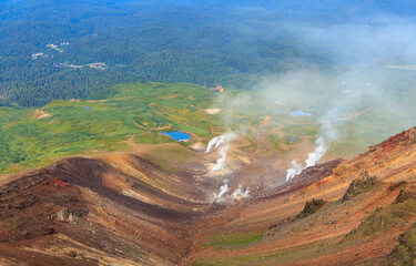 Steep volcanic slope with gas and steam vents above green meadows and treeline - 642121903