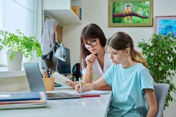 Mother helping preteen daughter to study, looking at laptop at home