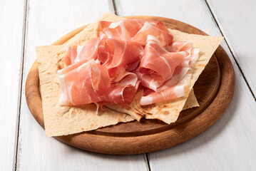 Fette di prosciutto crudo su pane carasau e tagliere in legno, cibo rustico italiano 
