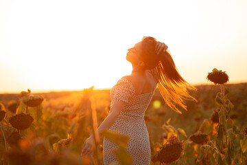 young woman in evening sunlight in a sunflower field at summer sunset, girl holding hands on hair...
