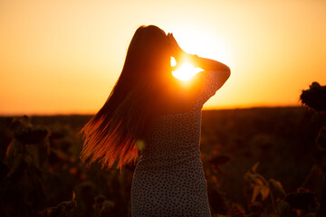 silhouette of young woman in a sunflower field during a beautiful summer sunset. Woman holding her...