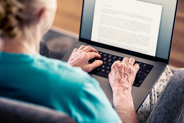 Old senior woman using laptop computer to write text. Book, testament, letter or journal. Elder...