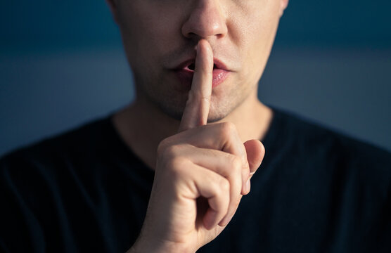 Secret and silence. Quiet silent shh gesture with finger on lips. Man doing expression with hand on mouth. Taboo topic, censorship or freedom or speech. Conspiracy theory. Confidential talk.
