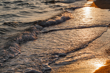 Sea surf on the sandy coast close-up, glare on the water from the setting sun