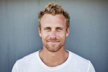 Blonde 40 year old man in white t-shirt standing against a grey wall.