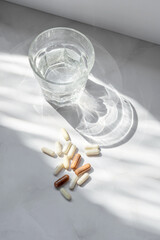 Glass with clean pure water and pills and capsule on white marble table background with aesthetic...
