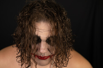 A scary clown looks into the camera frowningly on a black background. On halloween, a man in a...