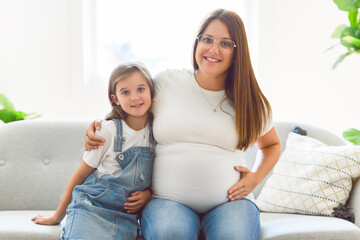 Excited little daughter touching pregnant mom tummy, standing next to window