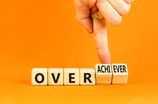 Achiever or overachiever symbol. Businessman turns wooden cubes and changes word Achiever to Overachiever. Beautiful orange background. Business achiever or overachiever concept. Copy space.